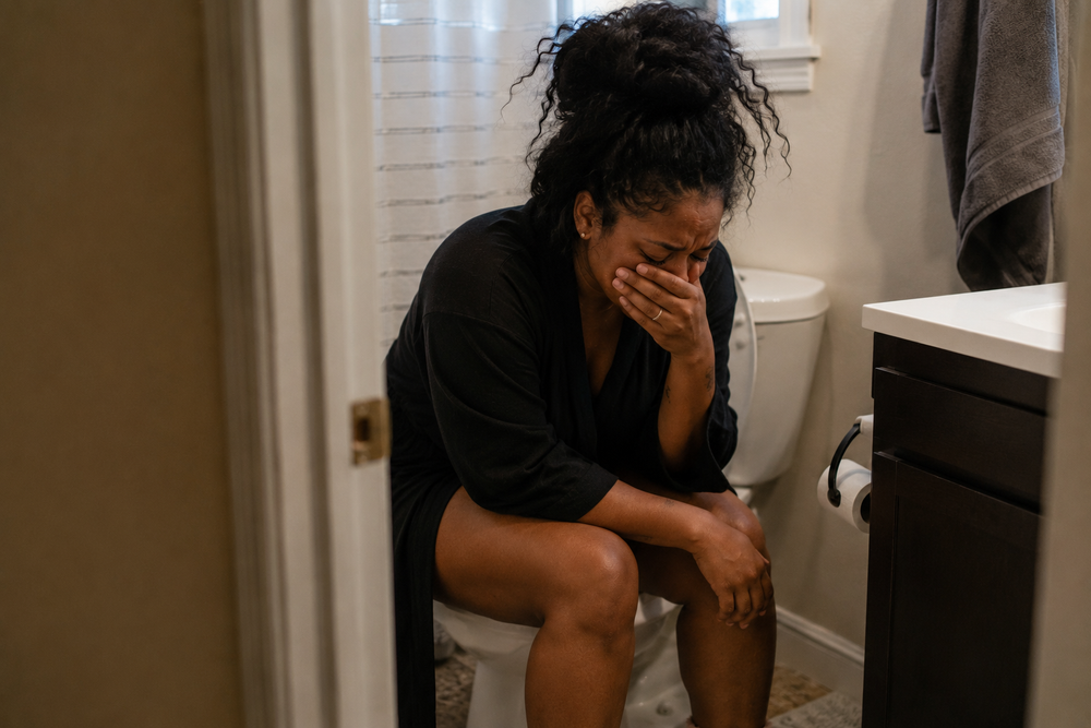 A postpartum mother sitting in a bathroom during recovery after vaginal birth, reflecting on the challenges of healing in the early days of motherhood.